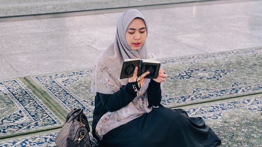 Oki Setiana Dewi sitting on a prayer mat while Umrah with Hijaberlin Handsock Palestine, reading the Qur'an